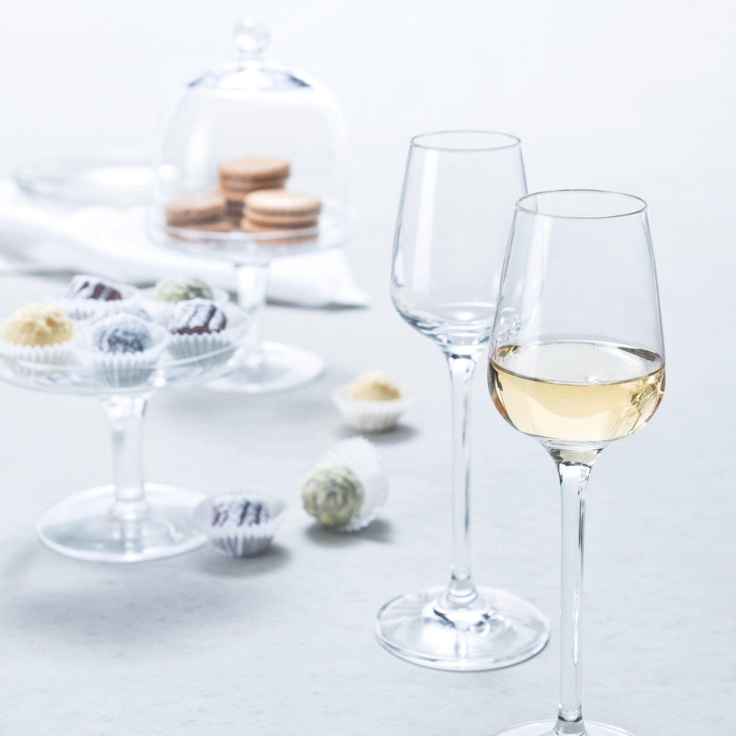 Zwei Digestifgläser TIVOLI mit Weißwein gefüllt auf gedecktem Tisch mit Süßspeisen