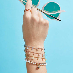 Hand mit mehreren goldenen Armbändern vor blauem Hintergrund