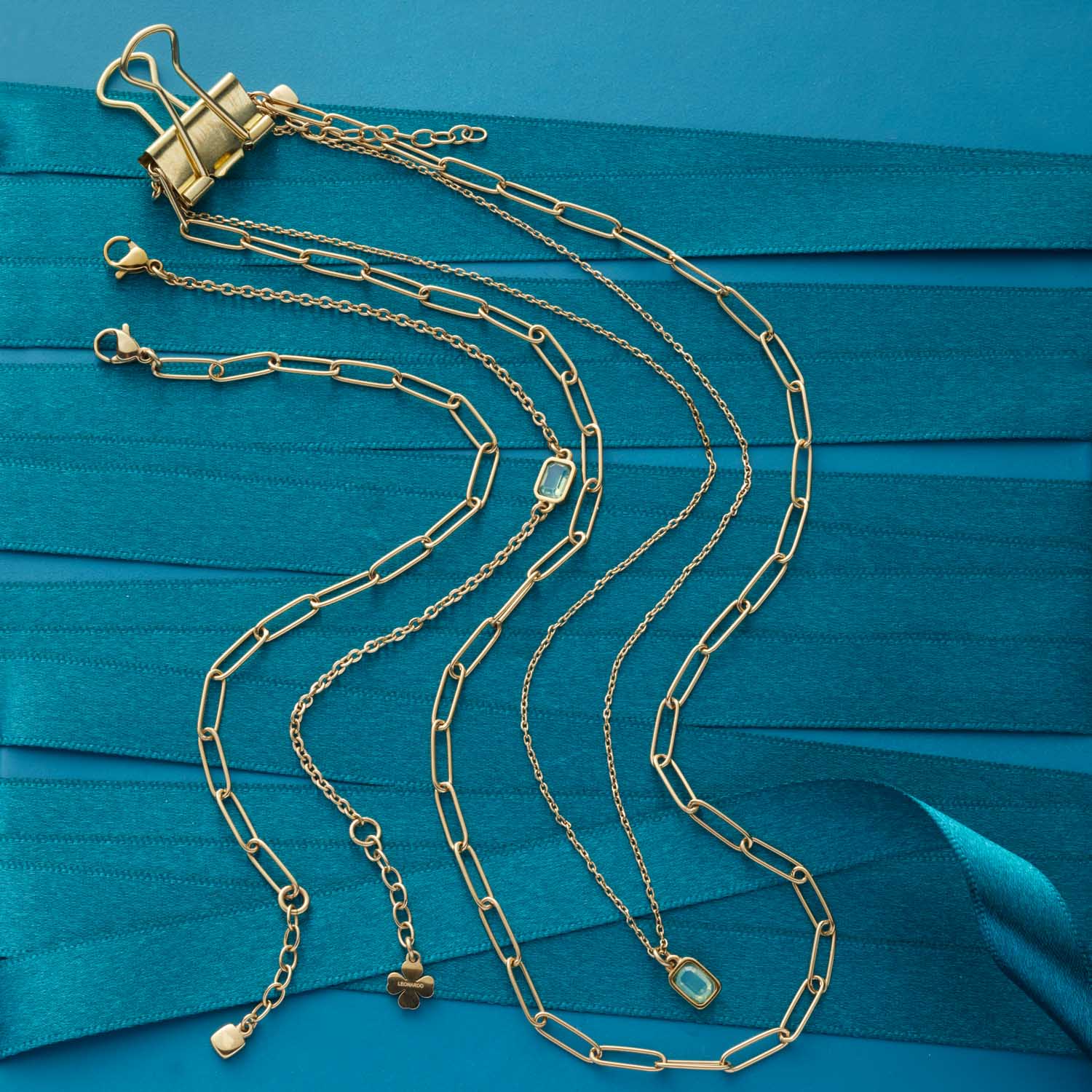 Mehrere goldene Ketten auf türkisblauem Hintergrund mit Binder-Clip