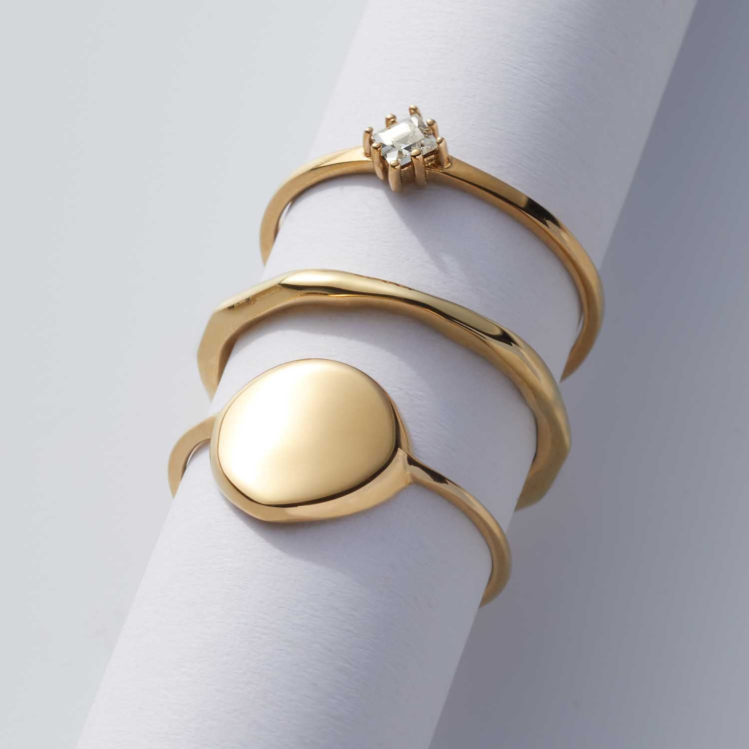 Goldene Ringe der Serie CIAO auf weißem Zylinder, darunter Ring PAVINA 16 CIAO mit ovalem Element