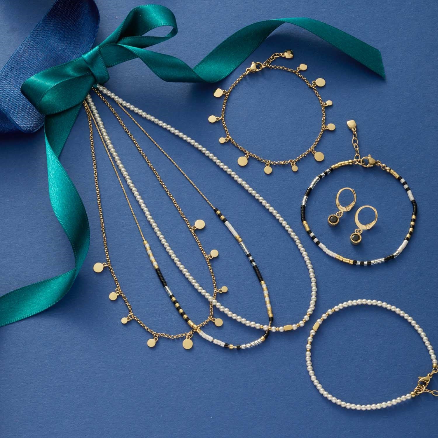 Halskette DORO mit Muscheln, Armbändern, Ohrringen und grünem Seidenband auf blauem Hintergrund