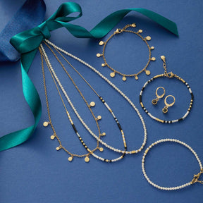 Schmuckkollektion mit Armbändern, Ohrringen und grünem Band auf blauem Hintergrund