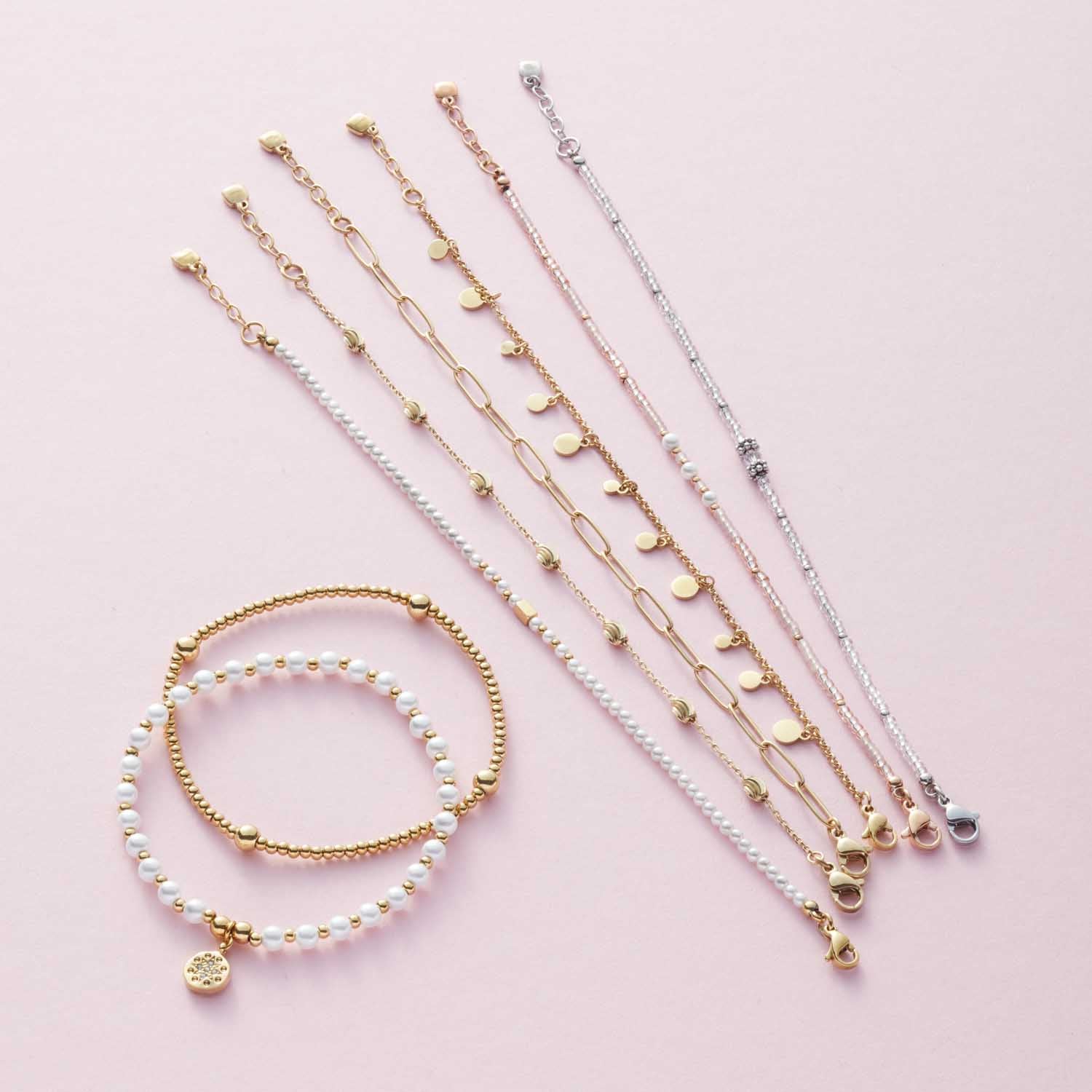 Mehrere Armbänder der Serie CIAO in Weiß und Gold auf rosa Hintergrund
