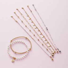 Mehrere Armbänder der Serie CIAO in Weiß und Gold auf rosa Hintergrund
