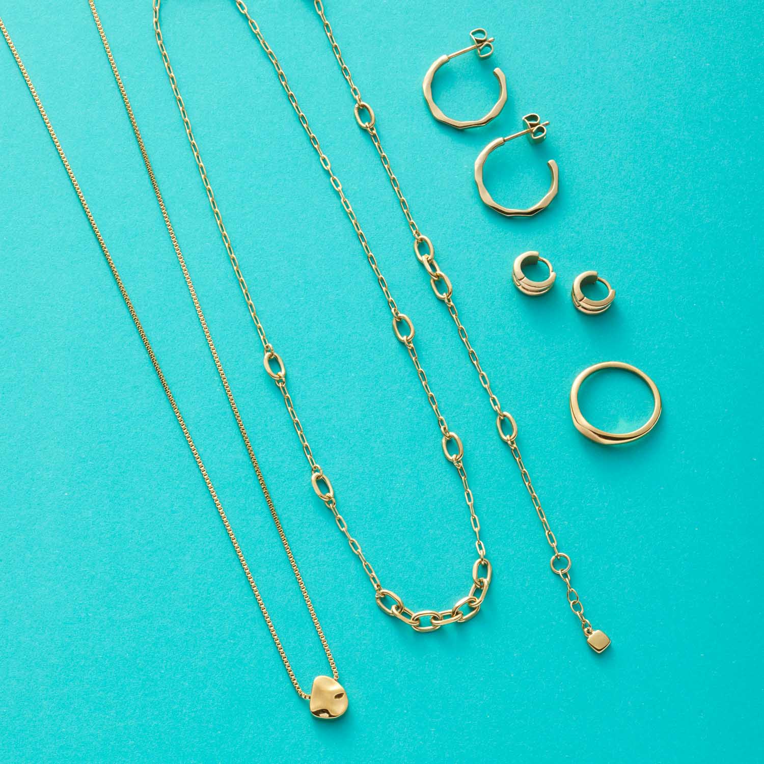 Goldene Schmuckkollektion mit Halsketten, Ringen und Ohrringen auf türkisem Hintergrund