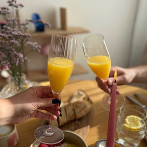 Zwei Sektgläser POESIA mit Orangensaft gefüllt, festlich gedeckter Tisch mit Kerzen