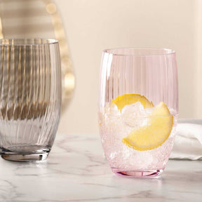Trinkglas POESIA rosé mit Zitronenscheibe und Eiswürfeln, neben grauem Glas auf Marmortisch