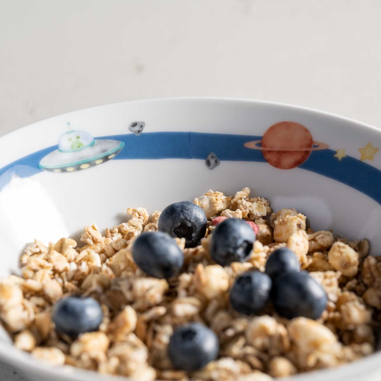Kindergeschirr BAMBINI AVVENTURA mit Weltall-Motiv gefüllt mit Müsli und Blaubeeren