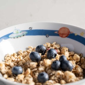 Kindergeschirr BAMBINI AVVENTURA mit Weltall-Motiv gefüllt mit Müsli und Blaubeeren