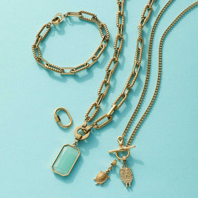 Anhänger MORA Clip & Mix in Gold mit passenden Ketten und Armband auf hellblauem Hintergrund
