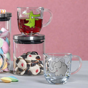 Tasse BAMBINI 280 ml Krokodil mit rotem Tee, daneben Elefantentasse und Süßigkeiten