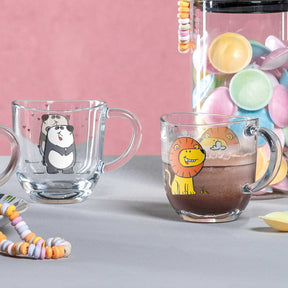 Glastasse BAMBINI mit Panda-Motiv, daneben Glastasse mit Löwen-Design, bunte Dekoration im Hintergrund