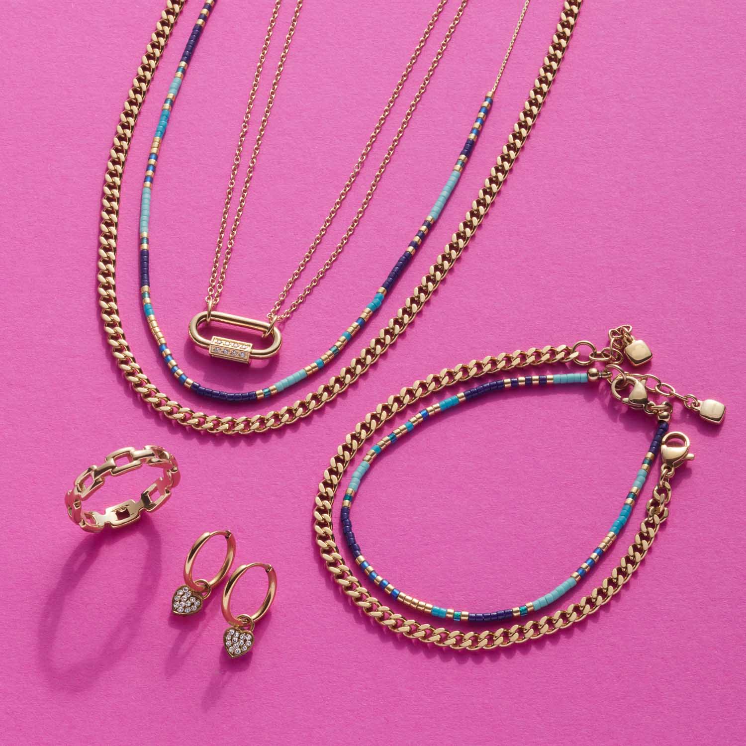 Goldene Halsketten, Armband und Ringe auf rosa Hintergrund