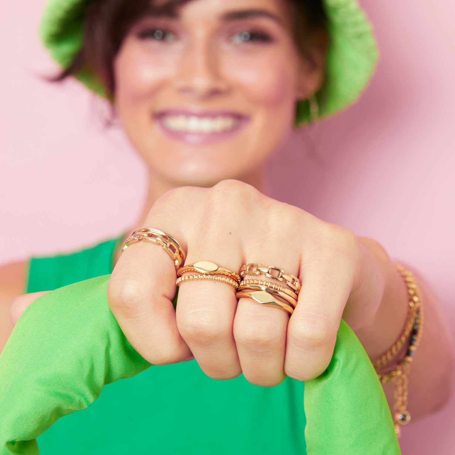 Frau trägt goldene Ringe ROCKY 16 CIAO an der Hand, grüner Hintergrund