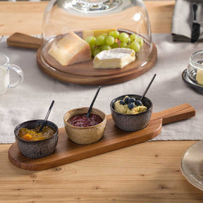 Servierbrett mit drei Dipschälchen auf gedecktem Tisch, Käse und Trauben unter Glasglocke