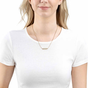Frau traegt goldene Halskette Pilea um den Hals, weisses T-Shirt