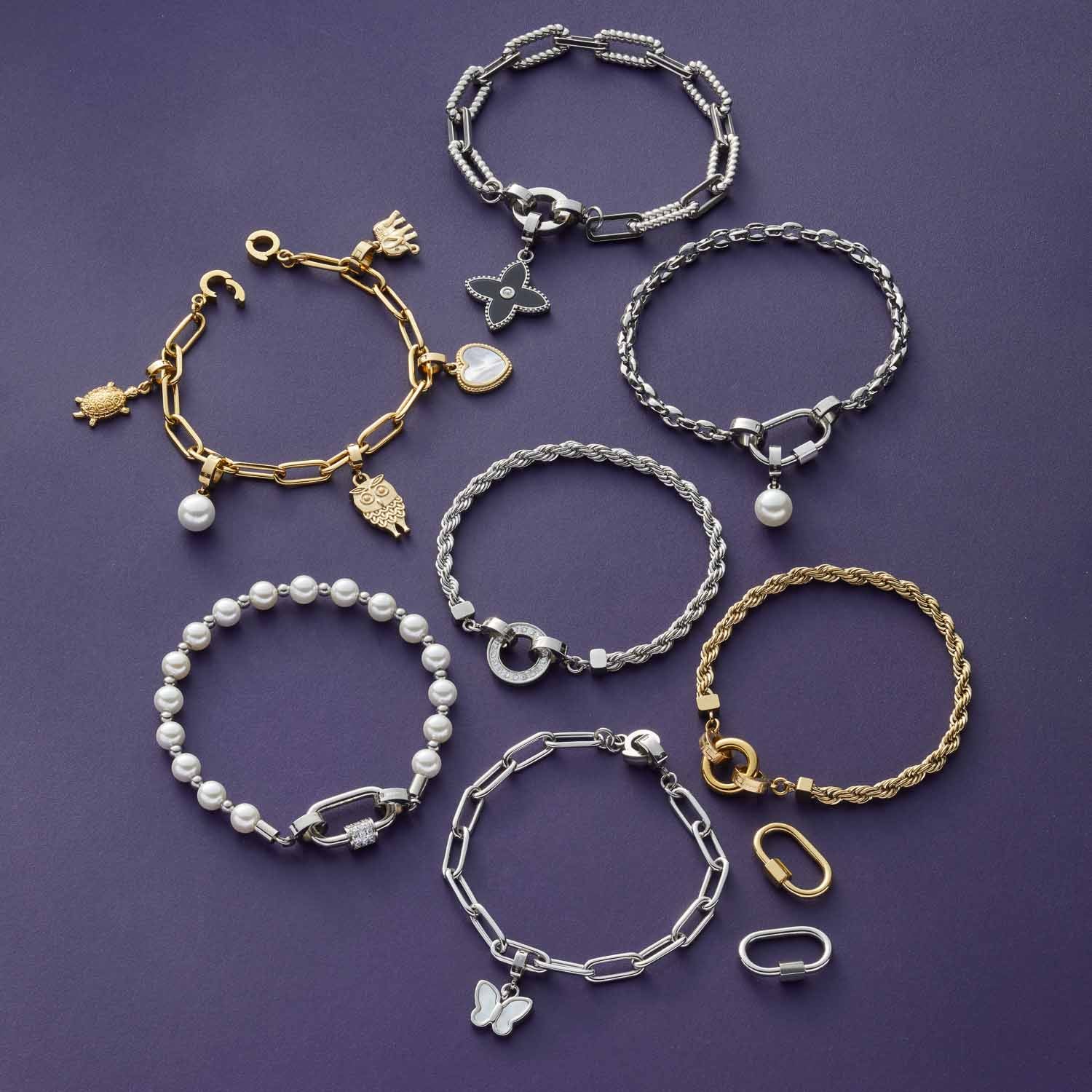 Acht Armbänder in Gold- und Silbertönen mit verschiedenen Anhängern auf violettem Hintergrund