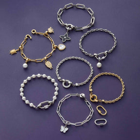 Acht Armbänder in Gold- und Silbertönen mit verschiedenen Anhängern auf violettem Hintergrund