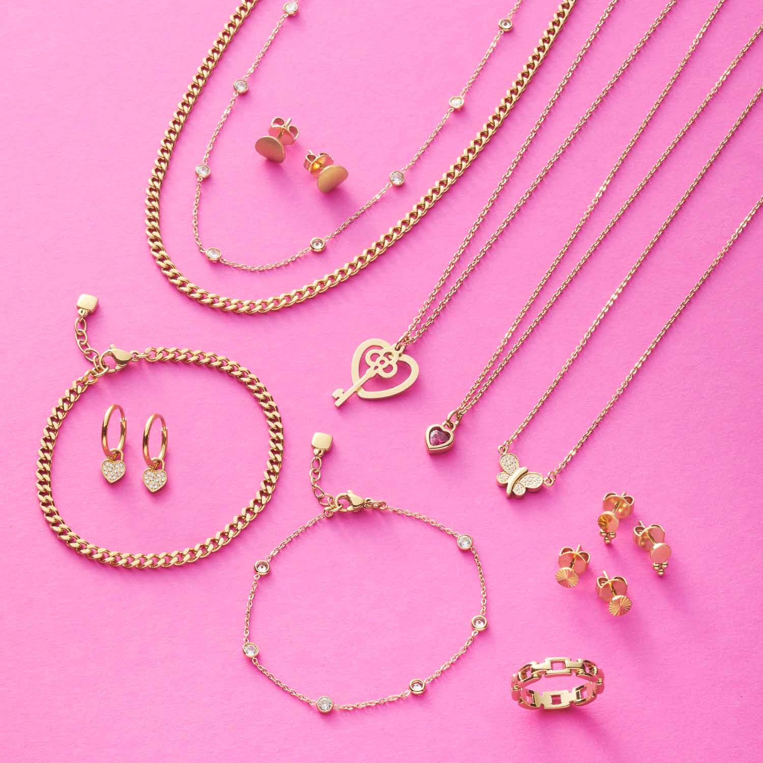 Goldene Schmuckkollektion mit Halsketten, Armbändern und Ohrringen auf rosa Hintergrund