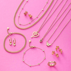 Goldene Schmuckkollektion mit Halsketten, Armbändern und Ohrringen auf rosa Hintergrund
