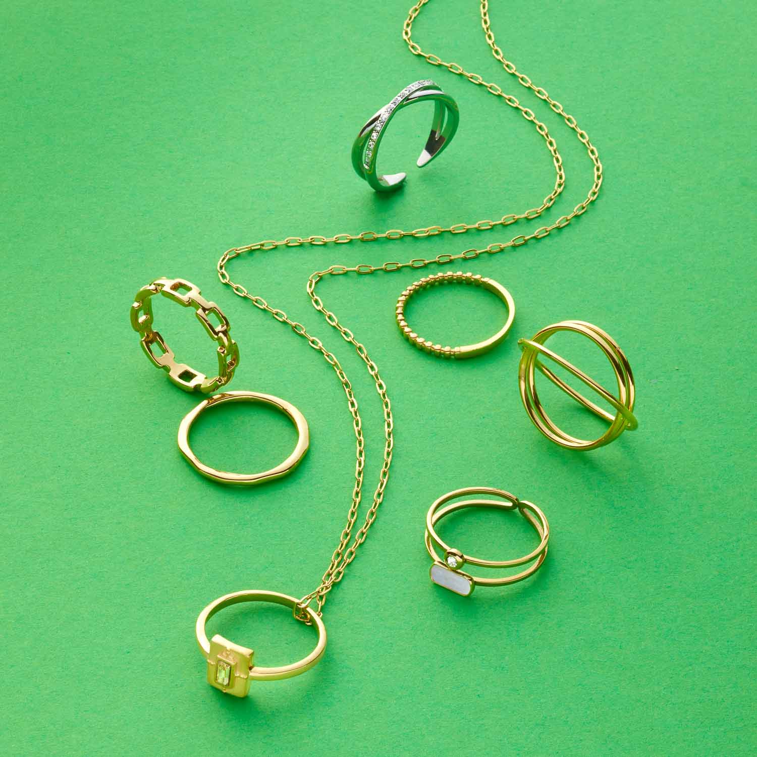 Goldene Ringe und Kette der Serie CIAO auf grünem Hintergrund arrangiert