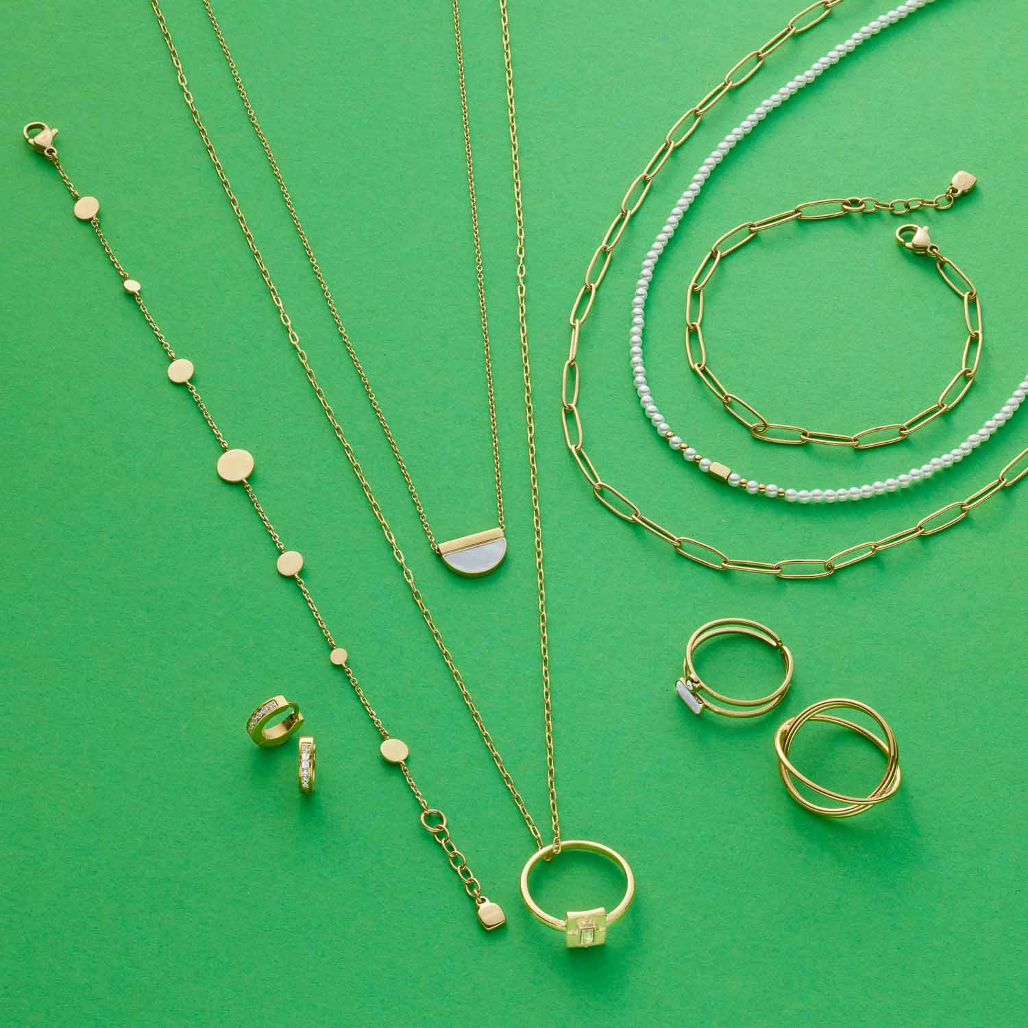 Goldene Schmuckkollektion mit Ringen, Ketten und Armbändern auf grünem Hintergrund