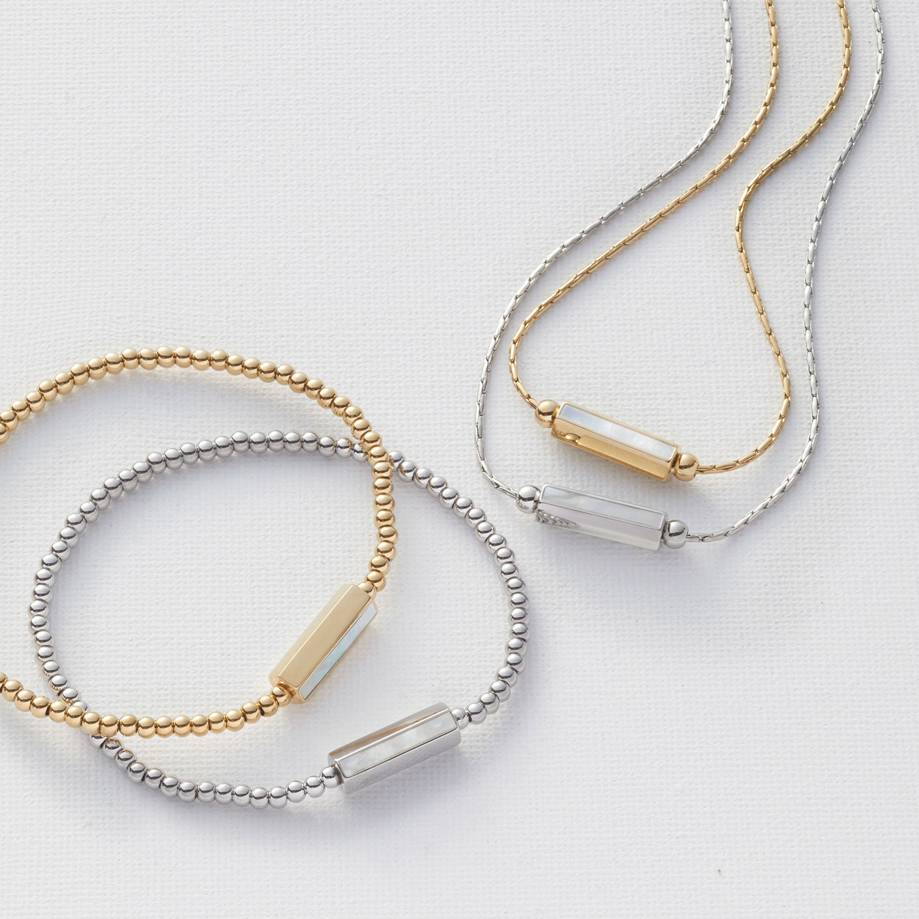 Armband PILEA gold und silber mit Perlenband und Metallzylinder auf weißem Untergrund