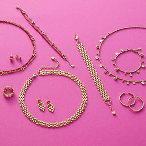 Schmuckkollektion aus Glasketten, Armbändern, Ohrringen und Ringen auf rosa Untergrund