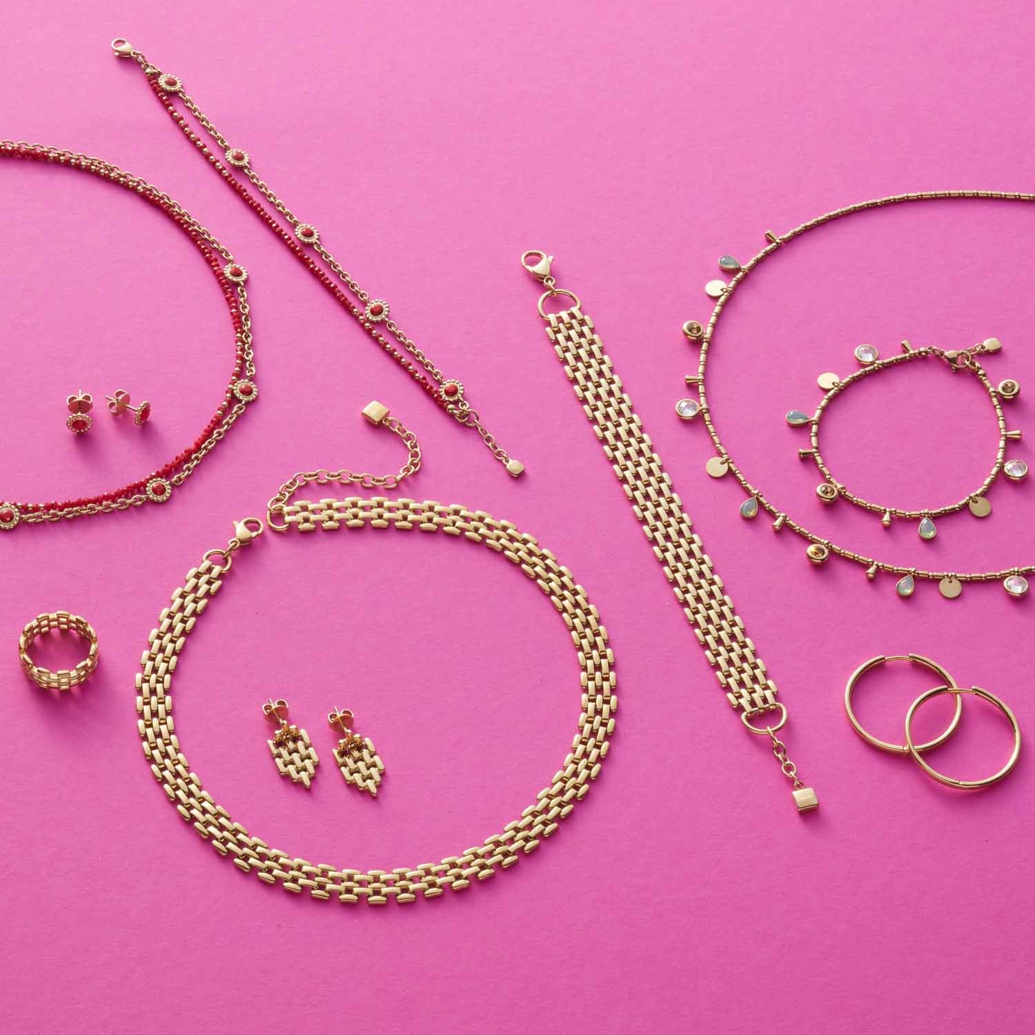 Goldene Schmuckstücke auf rosa Hintergrund arrangiert