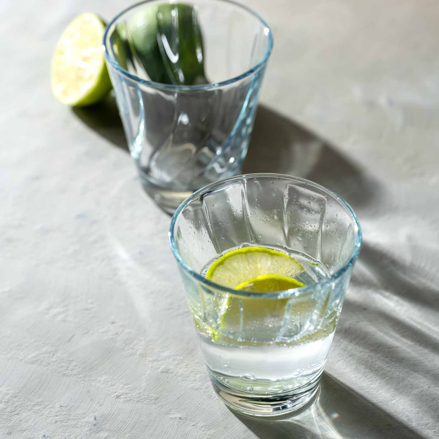 Zwei Trinkgläser TWIST mit Limettenscheiben und Eis auf grauem Untergrund