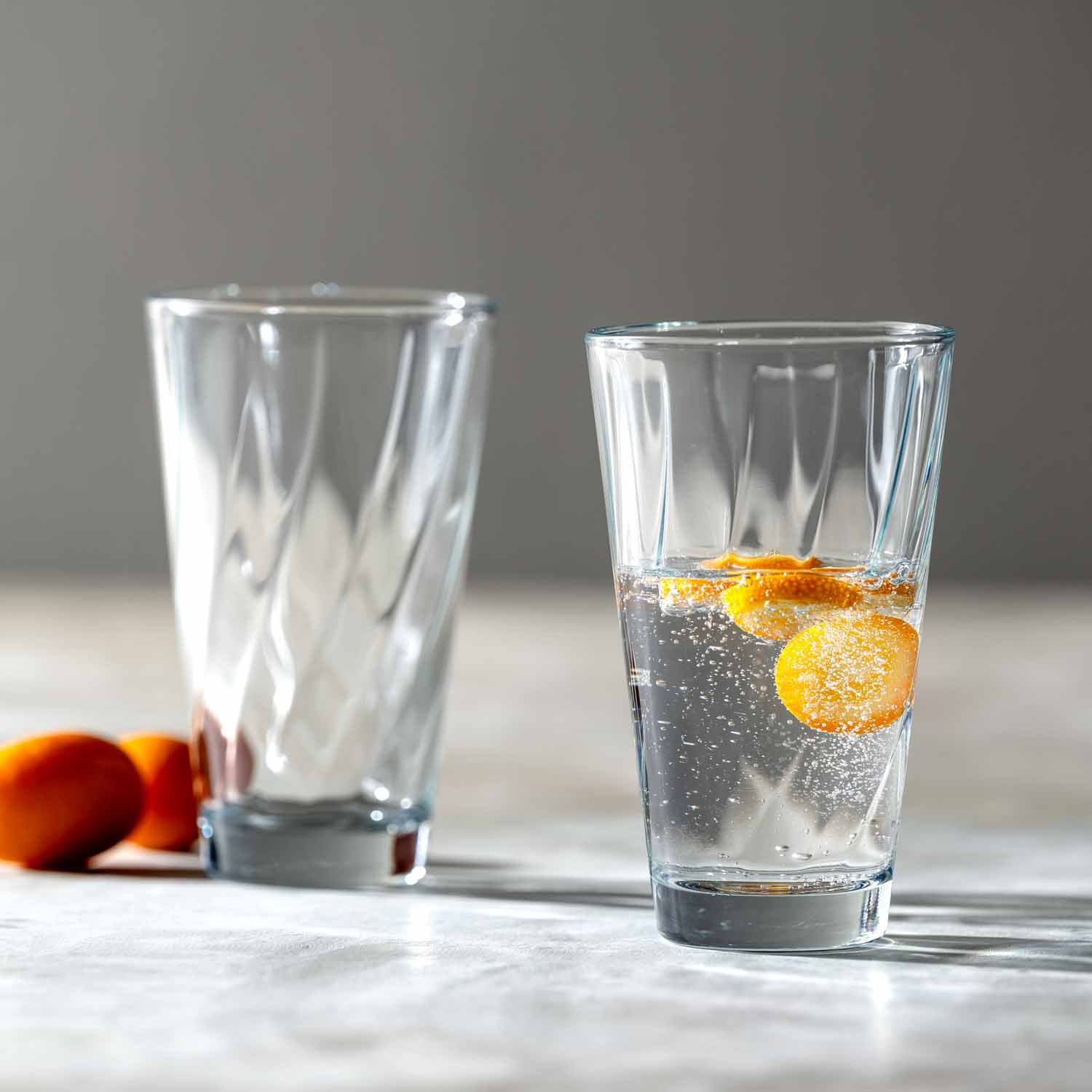 Zwei Trinkgläser TWIST, eines leer, eines mit Wasser und Zitronenscheibe gefüllt