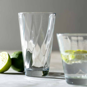 Trinkglas TWIST mit Limetten auf weißem Untergrund, gefülltes Glas im Hintergrund