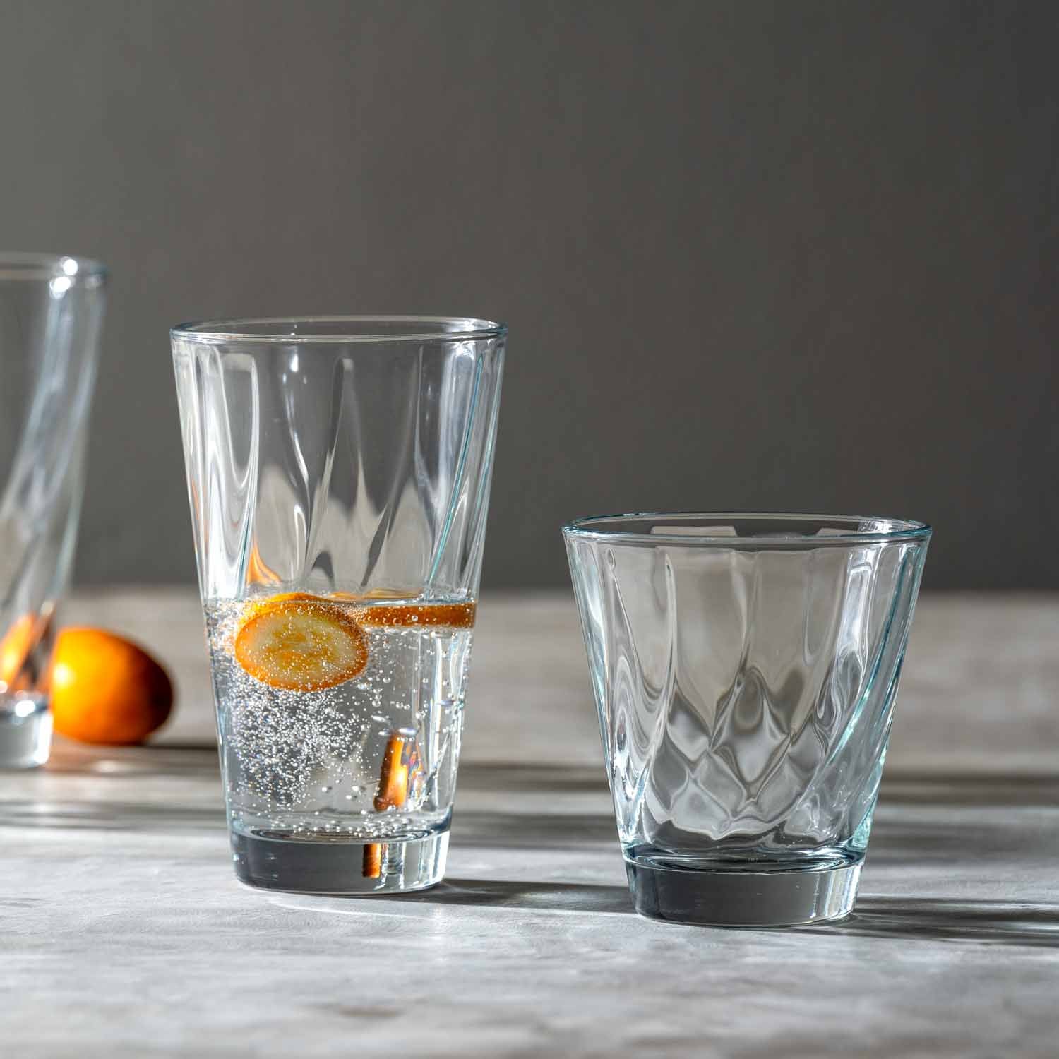 Trinkglasset TWIST mit Wasser, Eiswürfeln und Orangenscheibe auf Holztisch