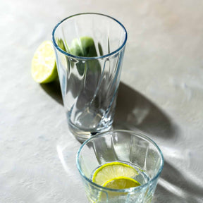 Zwei klare Glaeser der Serie TWIST mit Limettenscheiben auf grauem Untergrund