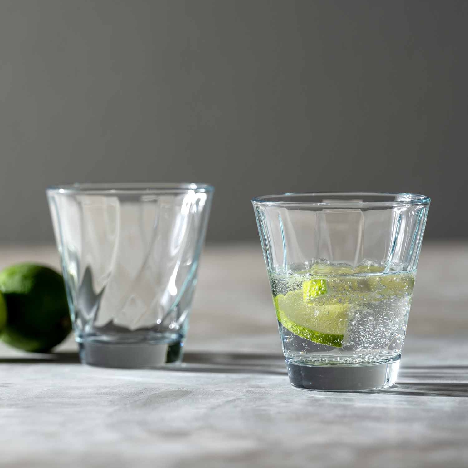 Zwei klare Glaeser auf Marmortisch, eines leer, eines mit Limette und Sprudelwasser gefuellt