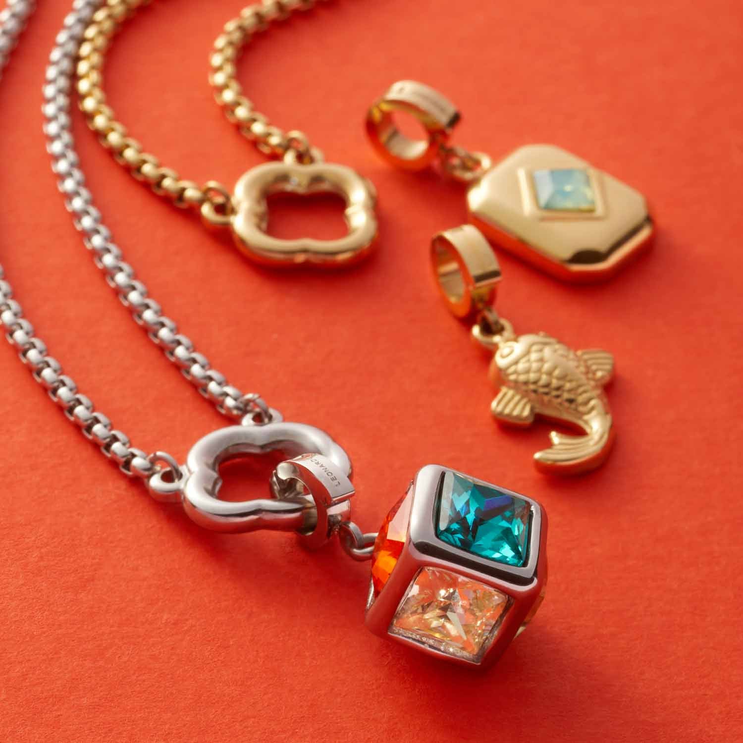 Anhänger ARI Clip & Mix in Gold und Silber auf orangerotem Hintergrund mit Ketten