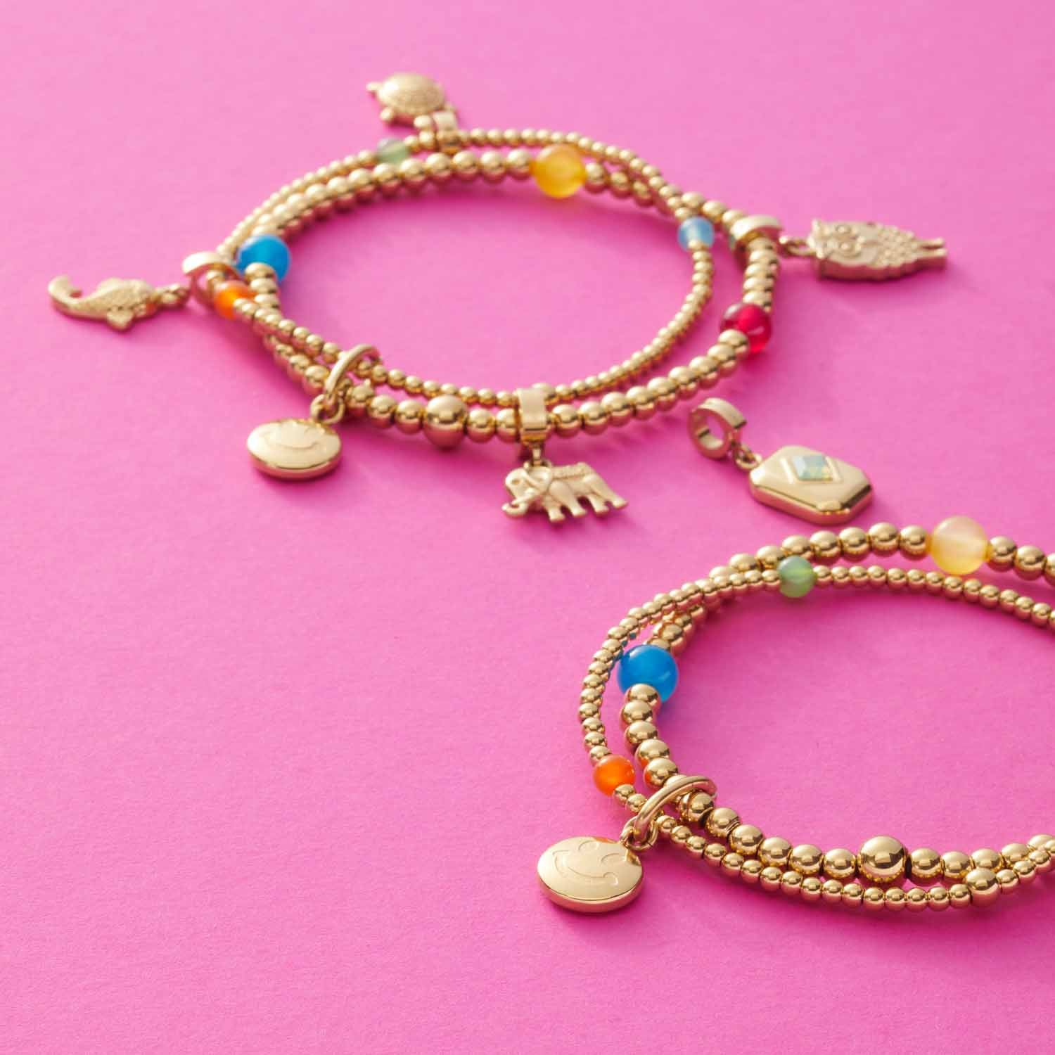 Zwei goldene Anhänger ARI Clip & Mix mit bunten Perlen und Charms auf rosa Hintergrund