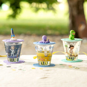 Drei Glasbecher mit Weltall-Motiven und farbigen Deckeln mit Figuren im Freien auf Tisch