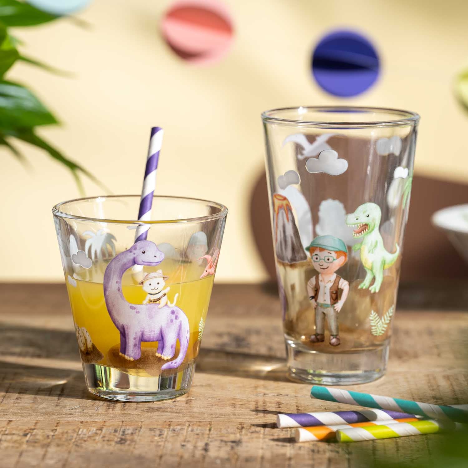 Trinkset BAMBINI AVVENTURA mit zwei Gläsern, farbigen Strohhalmen und Dino-Motiven auf Holztisch