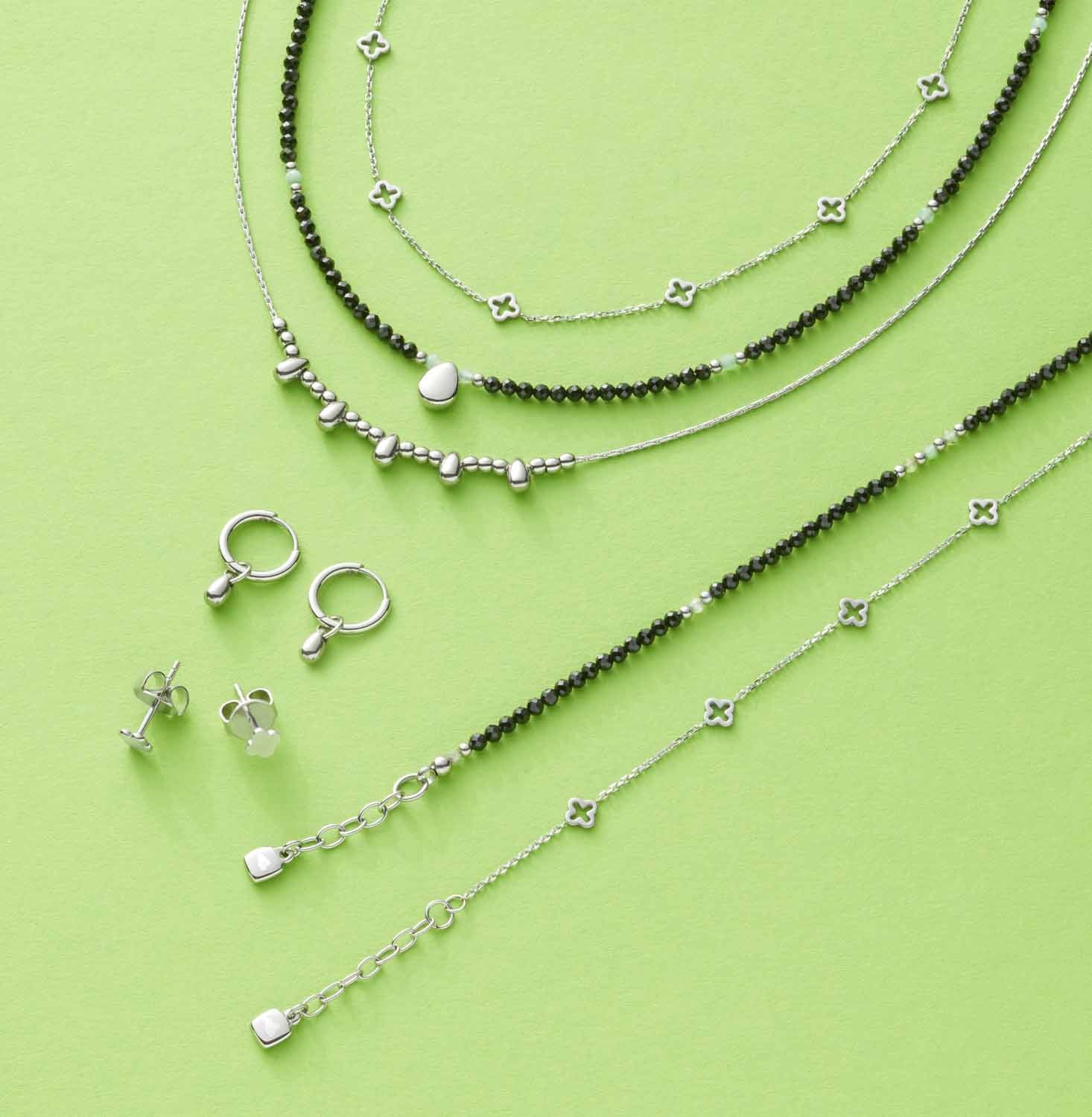 Silberne Halsketten, Ohrringe und Ringe auf grünem Hintergrund arrangiert