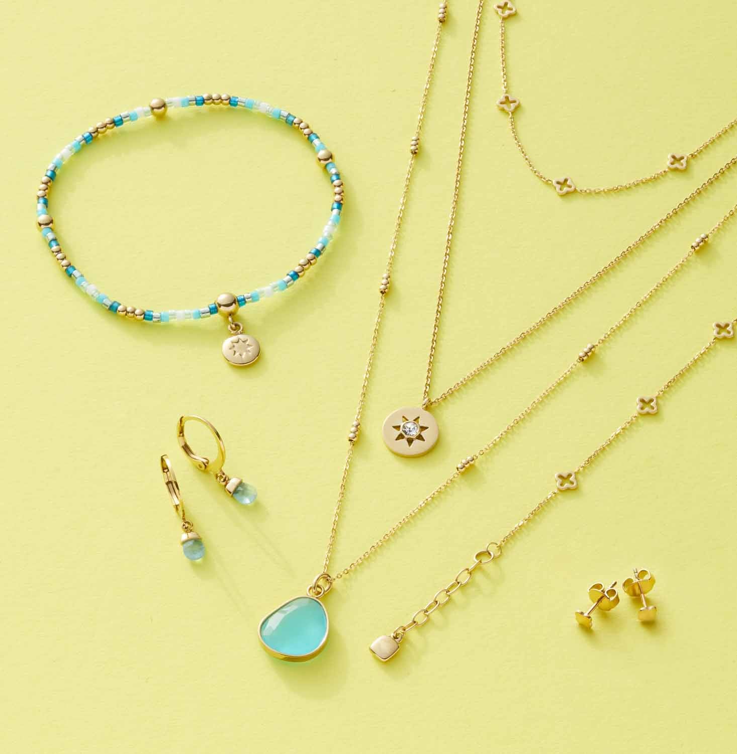 Schmuckkollektion mit Armbändern, Ketten und Ohrringen auf gelbem Hintergrund