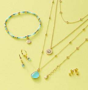Schmuckkollektion mit Armbändern, Ketten und Ohrringen auf gelbem Hintergrund