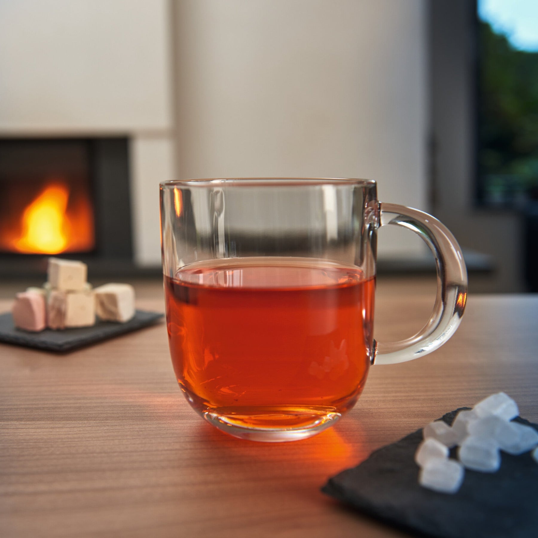 Glastasse MODENA mit rotem Tee, daneben Zuckerwürfel, Kamin im Hintergrund