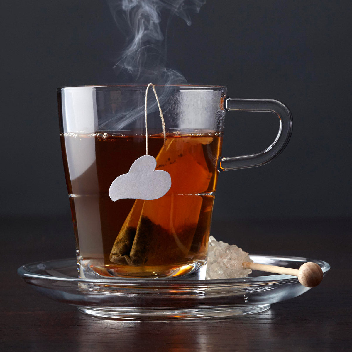 Glastasse mit Teebeutel auf Untertasse SENSO, dampfend, mit Zucker auf dunklem Hintergrund