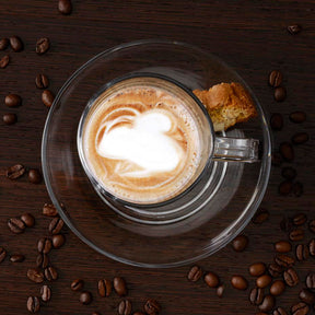 Untertasse SENSO mit Cappuccino und Keks, umgeben von Kaffeebohnen
