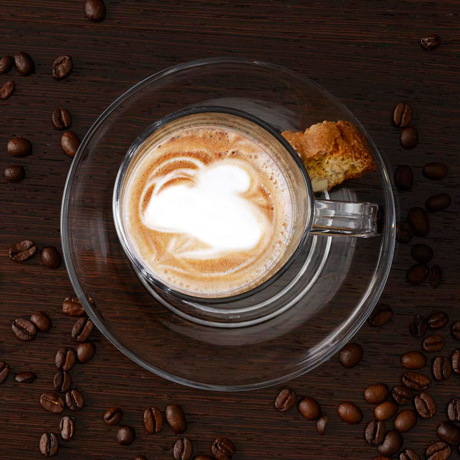 Untertasse SENSO mit Cappuccino und Keks, umgeben von Kaffeebohnen