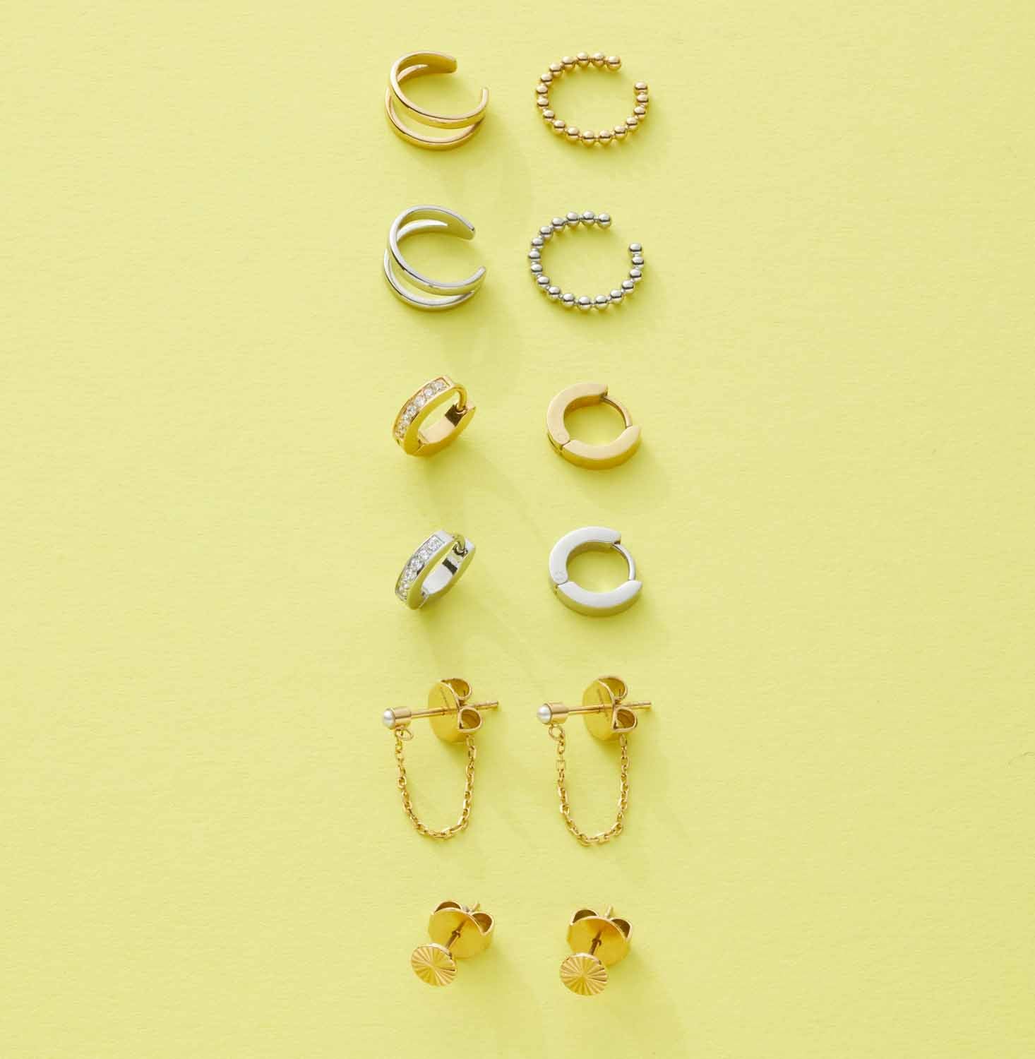 Verschiedene Ohrklemmen und Ohrringe in Gold und Silber auf gelbem Hintergrund