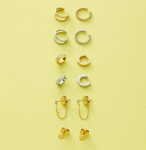 Verschiedene Ohrklemmen und Ohrringe in Gold und Silber auf gelbem Hintergrund