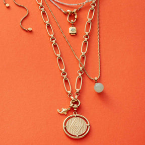Halskette MATHILDE 65 cm Clip & Mix in Gold mit mehreren Ketten und Anhängern auf orangem Hintergrund