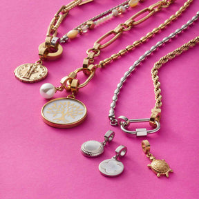 Armband MATHILDE Clip & Mix gold mit verschiedenen austauschbaren Anhängern auf rosa Hintergrund